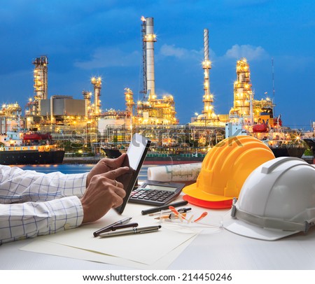 engineering working on computer tablet against beautiful oil refinery background