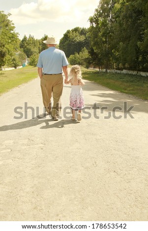 Grandfather with granddaughter walk along the road, - stock photo