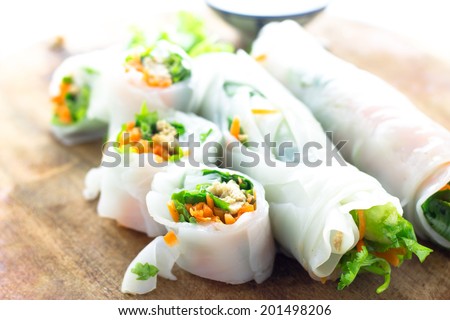 Portion of spring rolls on old wood with spicy sauce, vegetables and in noodle tube