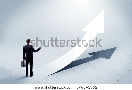 A young adult salesman standing in front of a big arrow pointing up with a shadow in grey empty space concept