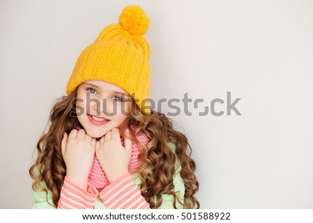 Cute little lady wearing yellow woolen cap and warm scarf against white background