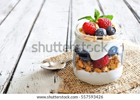 Healthy blueberry and raspberry parfait in a mason jar on a rustic white wood background