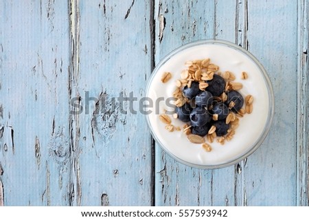 Greek yogurt with blueberries and granola, downward view on a rustic soft blue wood background