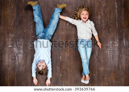 Happy children. Top view creative photo of little boy and girl on vintage brown wooden floor. Girl holding boy's leg. Boy is upside down