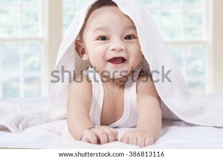 Portrait of excited male infant crawling and laughing on the bedroom under a white towel