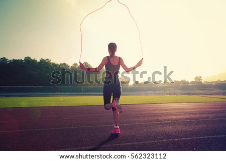 Young woman skipping rope during sunny morning on stadium track