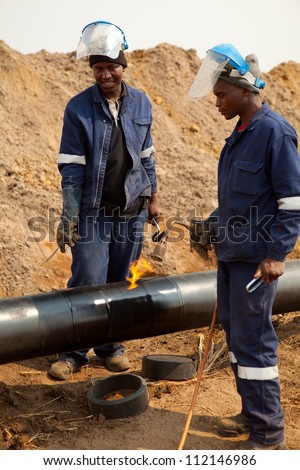 Male welder worker wearing protective clothing fixing welding and wrapping industrial construction oil and gas or water and sewerage plumbing pipeline outside on site