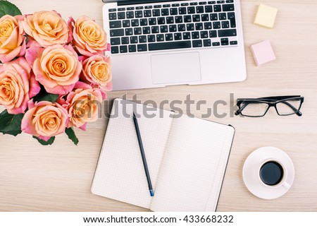 Top view of creative woman's desktop with open notepad, pencil, glasses, coffee cup, roses and laptop keyboard
