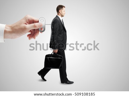 Mão girando enrolador nas costas do empresário.  Fundo cinza.  Conceito de controle