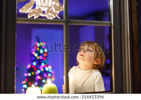 stock photo cute little boy looking at lights window at christmas time and holding candle with colorful lights 214453396