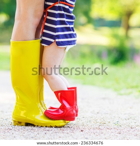 Legs of young woman and her little girl daughter in rain boots.