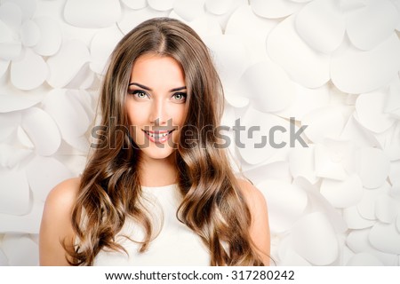 Beautiful tender woman in white dress posing by the background of white paper flowers. Beauty, fashion. Haircare. Cosmetics.