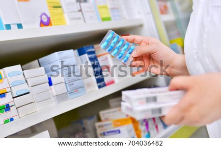 Pharmacist holding medicine box and capsule pack in pharmacy drugstore.
