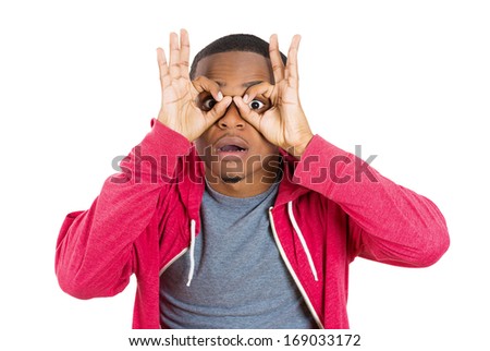 Closeup portrait of young handsome, surprised man looking through his fingers like binoculars, searching for something, looking to the future at the camera, isolated on a white background. Positive