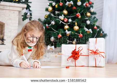 Little girl writes letter to Santa near christmas tree