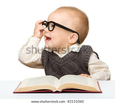 Cute little child play with book and glasses while sitting at table, isolated over white
