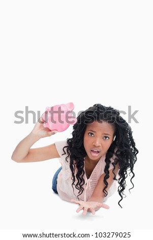 A worried young woman is holding an empty piggy bank against a white background