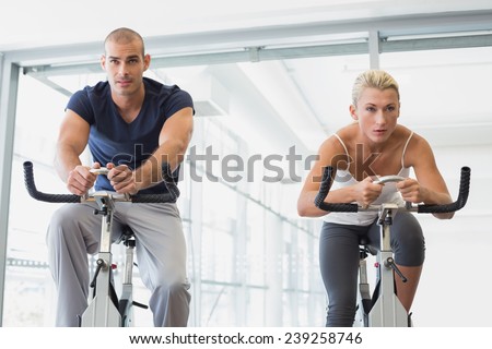 Determined fit young couple working on exercise bikes at the gym