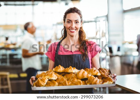 Baker showing tray of fresh croissant in the kitchen of the bakery