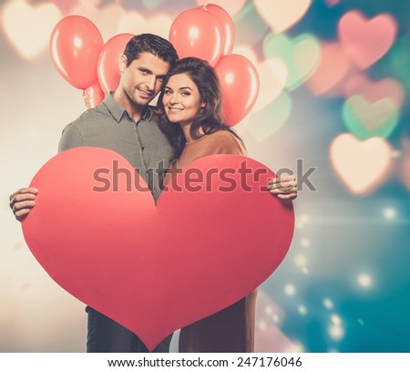 Couple holding handmade paper heart and red balloons