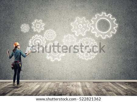 Back view of engineer woman in hardhat and sketched concept of teamwork on wall