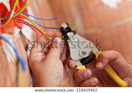 Electrician peeling off insulation from wires - closeup on hands and pliers