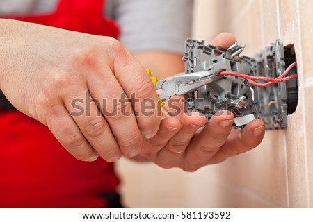 Electrician mounting the wires into electrical wall fixture or socket - closeup on hands and pliers