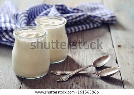 Greek yogurt in a glass jars with spoons on wooden background