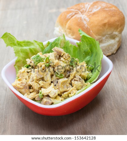 A savory curried chicken salad on lettuce with bun in background.