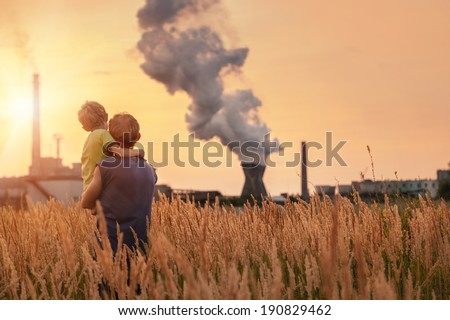 Ecological concept image. Father with son looking on chemical plant emissions at sunset time