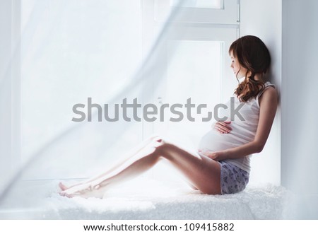 young pregnant woman sitting on the window