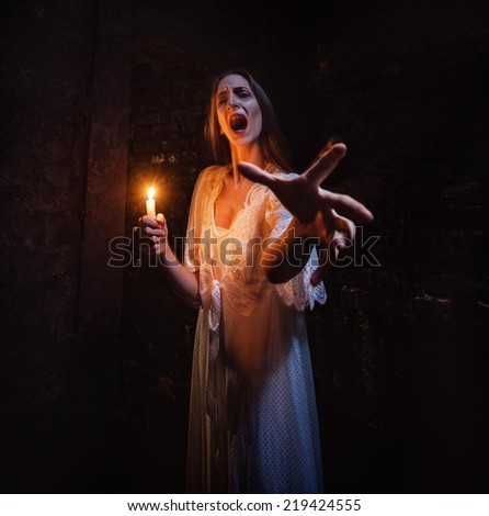 Scary woman standing in a dark hallway with lighten candle and screaming. Scary woman standing in a dark hallway with lighten candle and screaming.