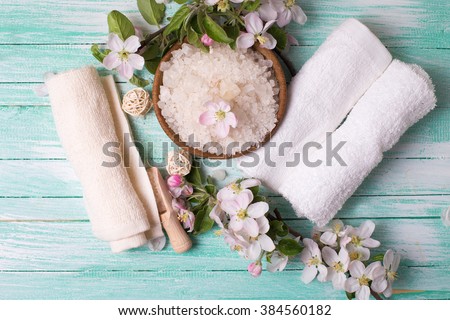 Spa or wellness setting. Sea salt in bowl, towels and apple blossom on turquoise painted wooden background. Selective focus is on salt.