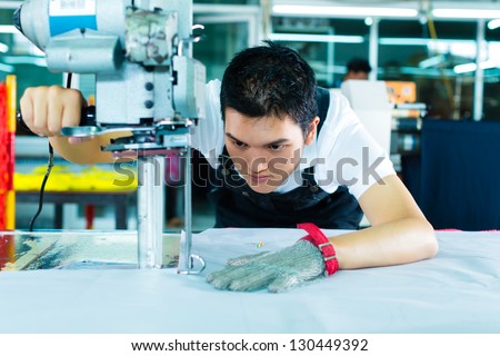 worker using a cutter - a large machine for cutting fabrics- in a Chinese textile factory, he wears a chain glove