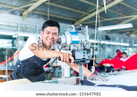 Indonesian worker using a cutter - a large machine for cutting fabrics - in a asian textile factory, he wears a chain glove