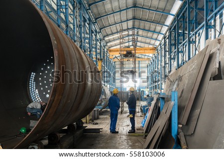 Two workers wearing yellow hard hat and blue uniform in the interior of an industrial hall