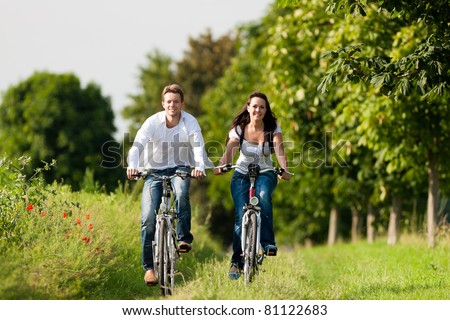 Happy young couple - man and woman - cycling in summer in nature