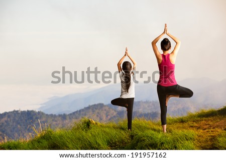 Mother and daughter doing yoga Tree pose at top of mountain