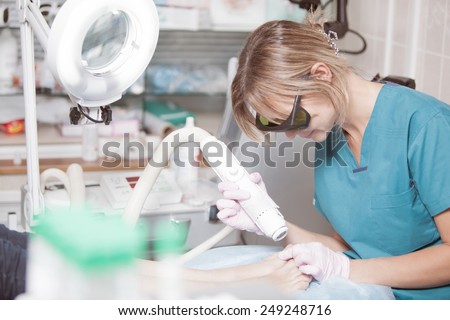 Nữ cosmetician trong kính an toàn tại nơi làm việc. Cô được điều trị bàn chân tốt với một laser