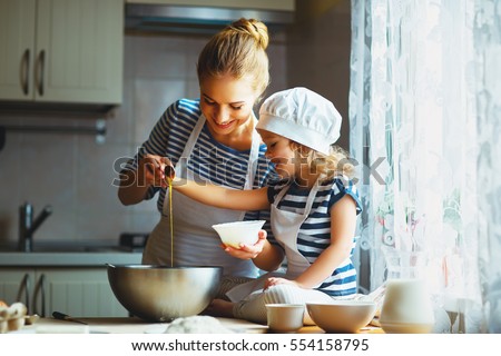 A woman and a child, both wearing blue and white striped shirts, in a bright kitchen adding ingredients to a large silver bowl. 