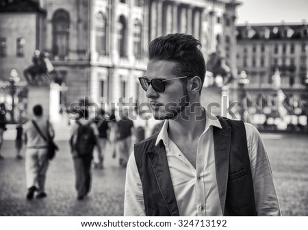 Waist Up Portrait of Fashionable Young Man Wearing Sunglasses and Standing Outdoors in Historical City Square and Gazing with Serious Expression to the Side