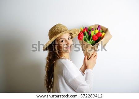 Beautiful spring woman in a hat holding a bouquet of colorful spring flowers. The concept of International Women's Day