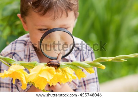 Happy little boy playing in the park with snail at the day time. He having fun on the garden. Concept of the kid is ready to go to school.