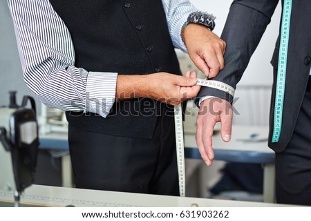 Closeup shot of old-fashioned tailor taking wrist measurements from client in small atelier studio to make custom classic suit with jacket