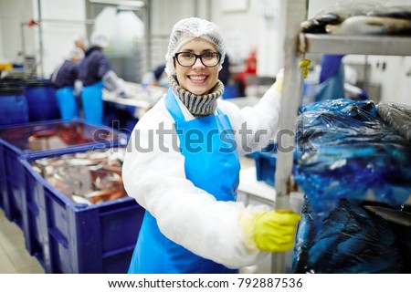 Smiling staff of seafood processing plant pushing huge cart with packed fish