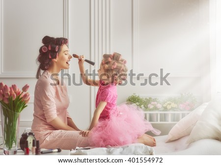 Happy loving family. Mother and daughter are doing hair and having fun. Mother and daughter doing your makeup sitting on the bed in the bedroom.
