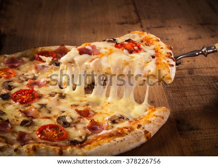 Hot pizza slice with melting cheese on a rustic wooden table.