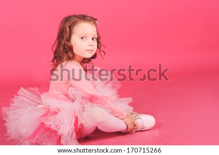 Cute baby girl sitting on the floor wearing pink dress at pink background in studio