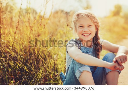 happy child girl in jeans overall playing on sunny field, summer outdoor lifestyle, cozy mood