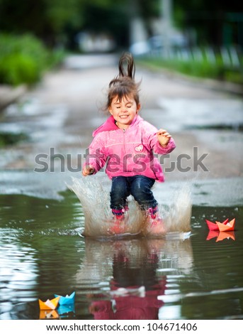 happy little girl, wearing a pink jacket, jumps into a puddle